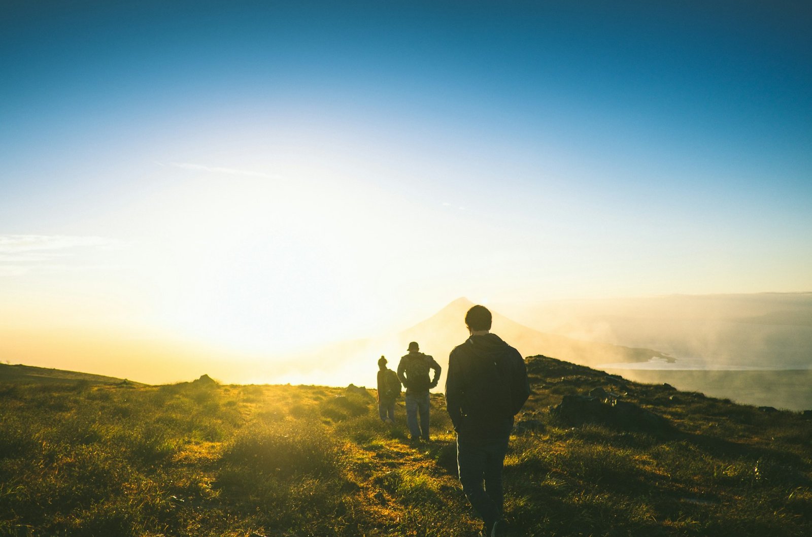 Three men hiking together toward a glowing sunrise on a mountain ridge