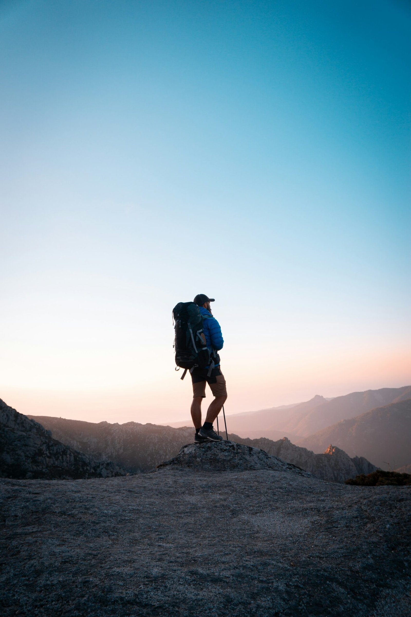 A hiker with a backpack standing on a rocky peak at golden hour