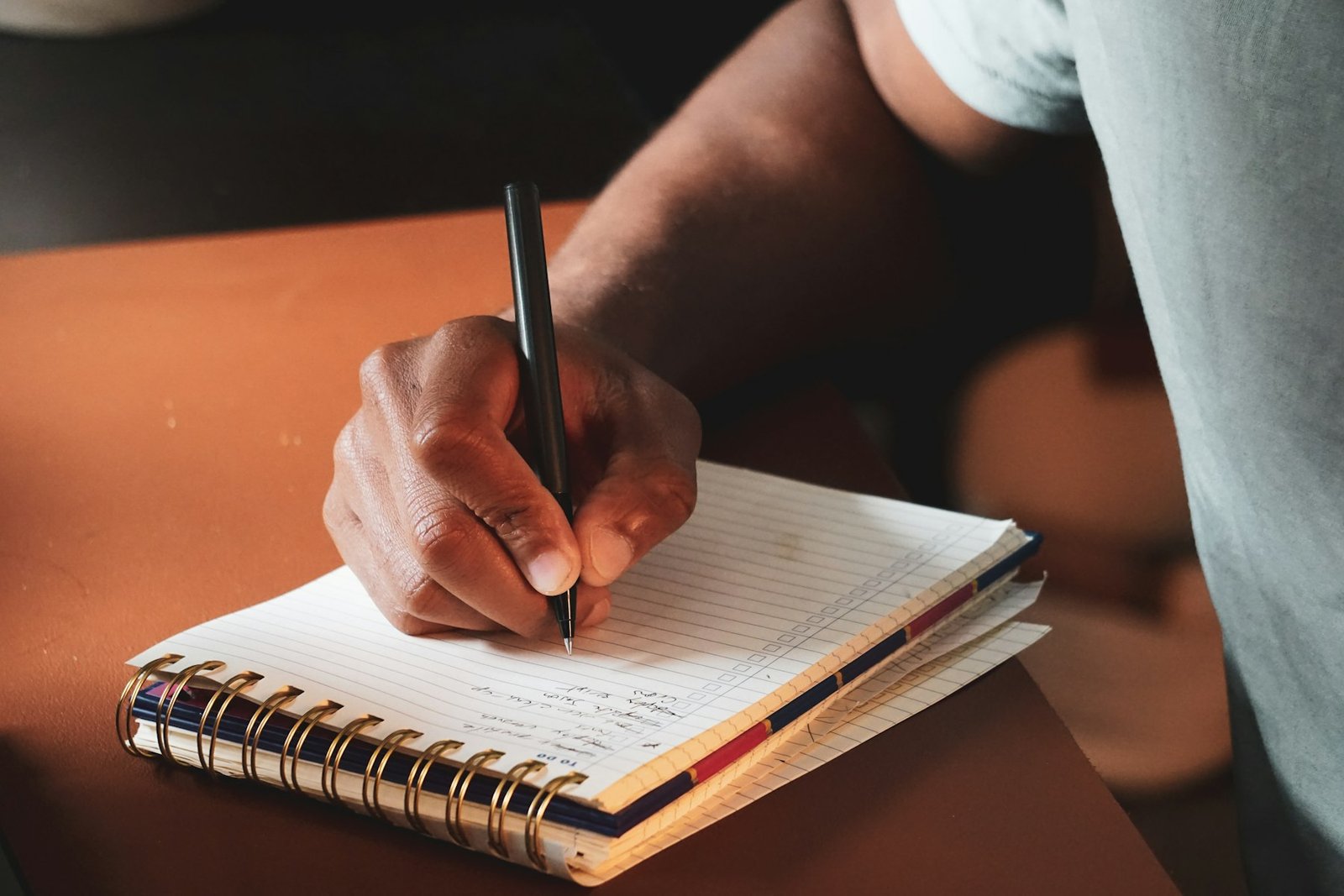 A hand writing in a spiral notebook with a pen