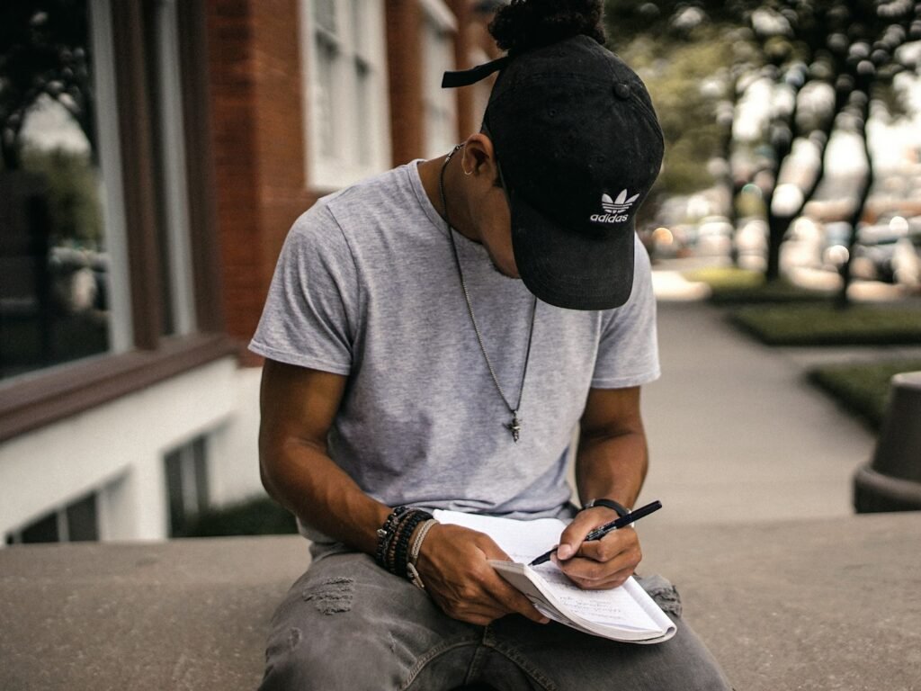 A man in a cap sitting outdoors writing in a notebook