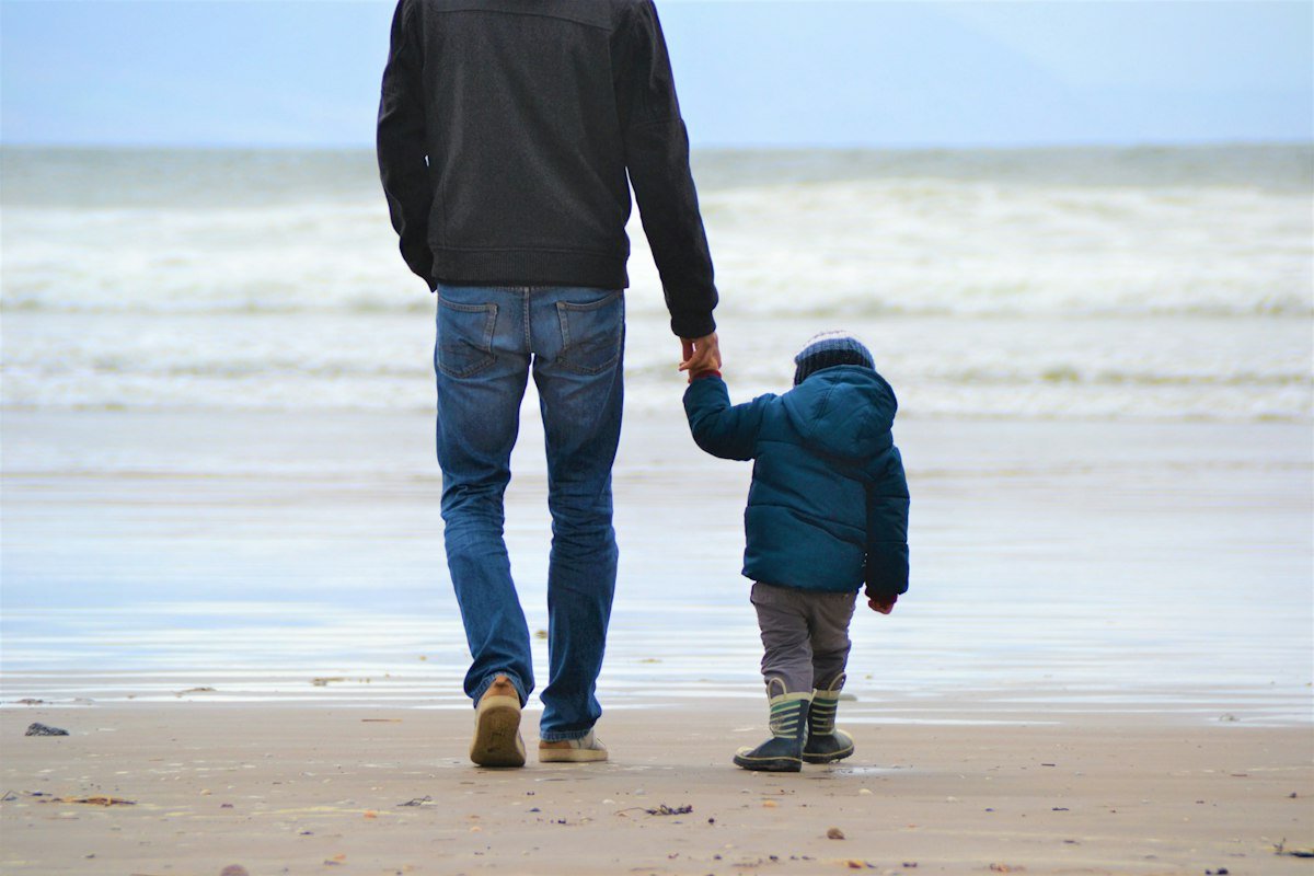 A father walking hand in hand with his young son along a beach